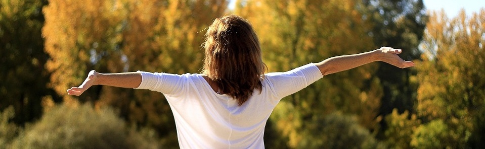 Woman standing in front of trees with her arms out, basking in the sun.