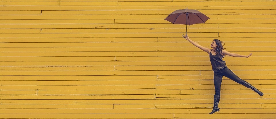 Woman holding umbrella floating in front of yellow wall.